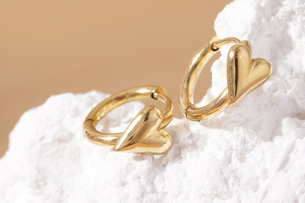Gold heart-shaped earrings on a textured white surface with a beige background