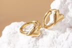 Gold heart-shaped earrings on a textured white surface with a beige background